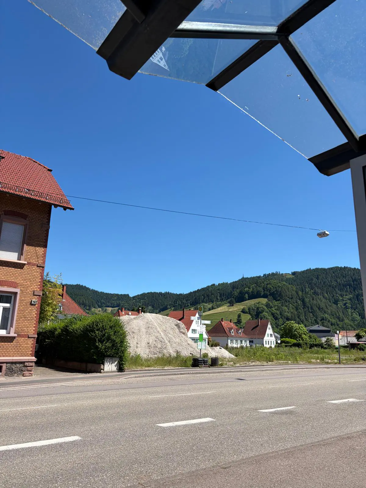 Village street and wooded hills from under a bus stop canopy